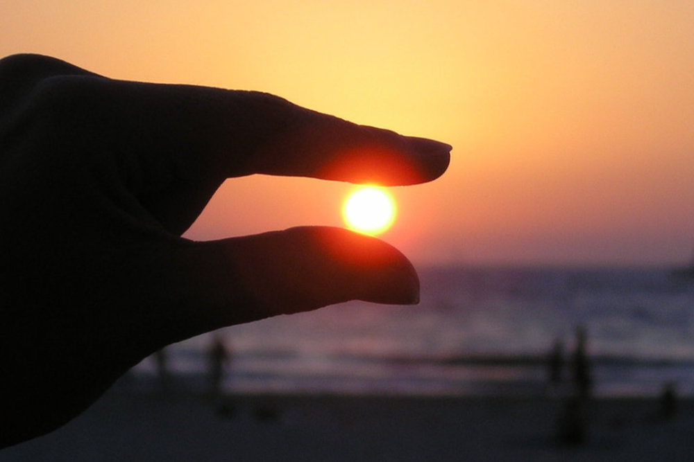 Hand pinching setting sun in perspective view