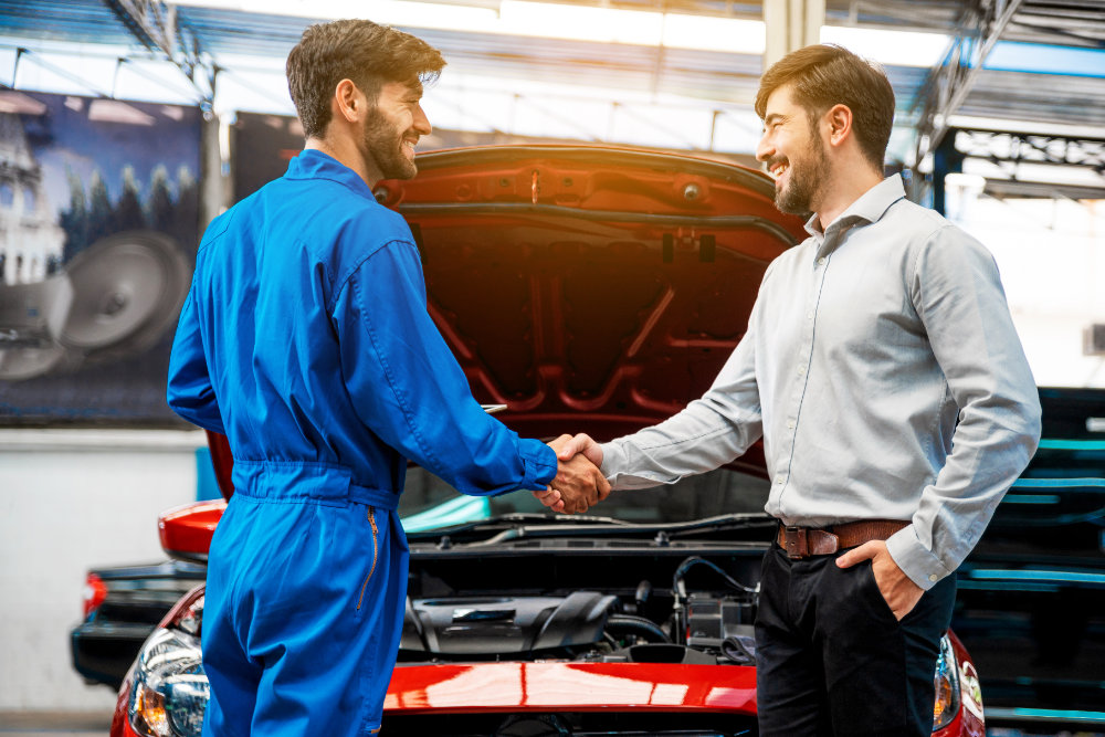 happy customer shakes hand of car maintenance worker in front of red vehicle in Canada