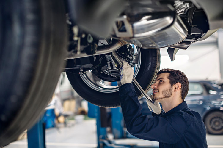 Car technician with wrench working beneath vehicle in Canada